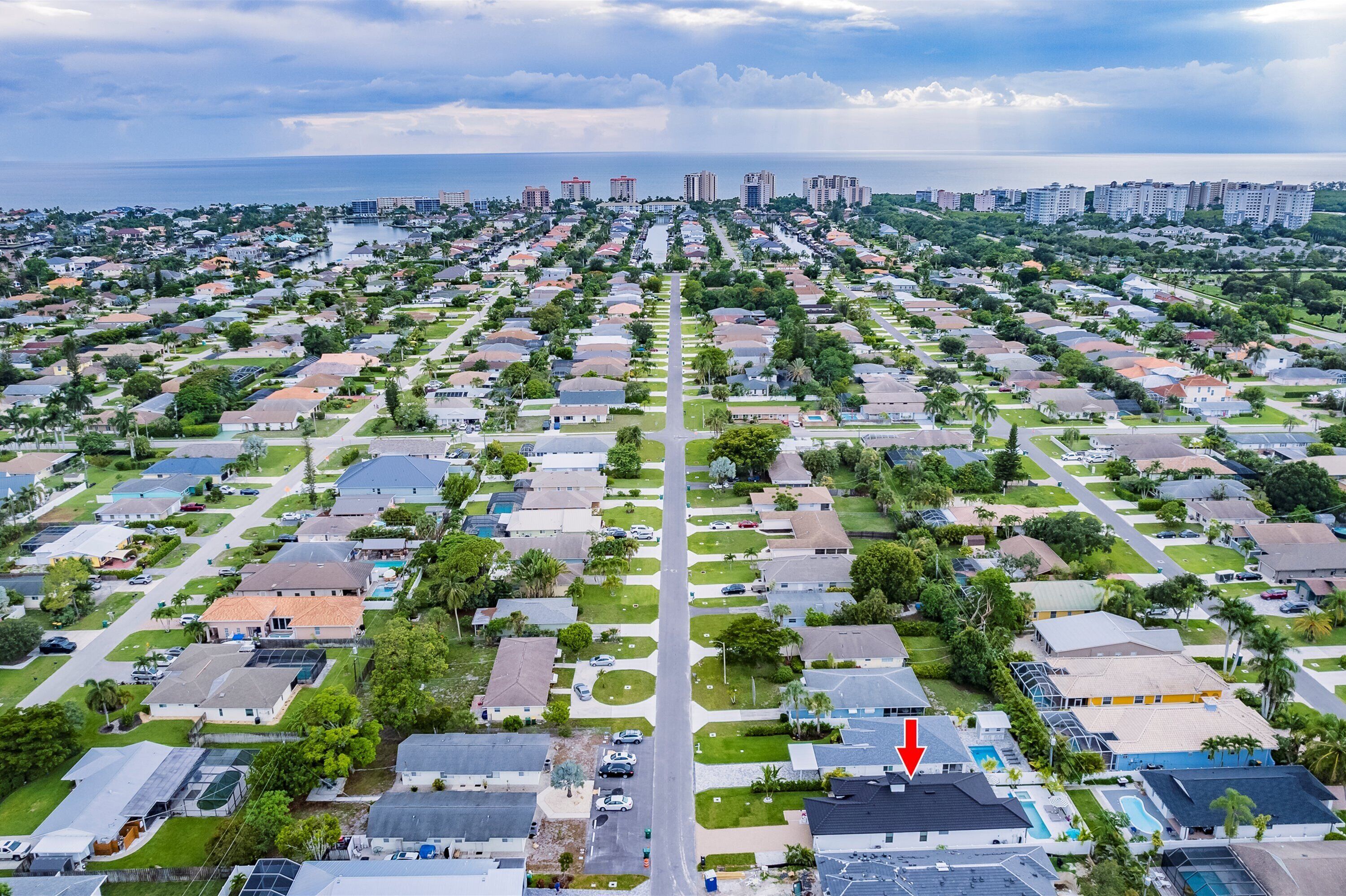 An aerial view of a residential area with a central road, houses, and a body of water in the background.