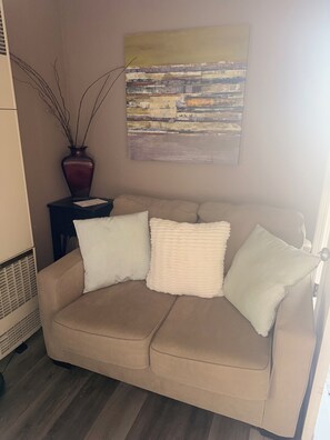 Un sofá color beige con tres almohadones, un florero con ramas y un cuadro en la pared.