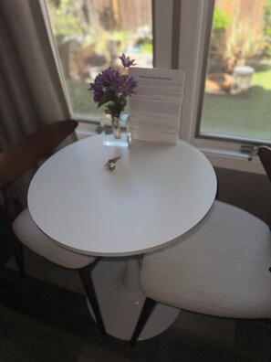 Una mesa redonda blanca con un pequeño florero de flores moradas, una llave y un menú encima.