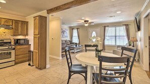 A modern kitchen with wooden cabinets, a dining area with a round table and chairs, and a living room with a sofa and a ceiling fan.