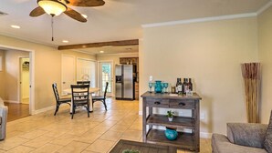 A spacious living room with a ceiling fan, a dining area with chairs and a table, a kitchen with a refrigerator, and a coffee table with a plant.