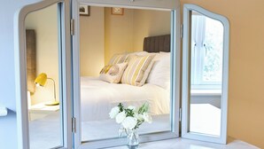 Ein Zimmer mit einem Bett, einem Schminktisch und einer Vase mit Blumen.