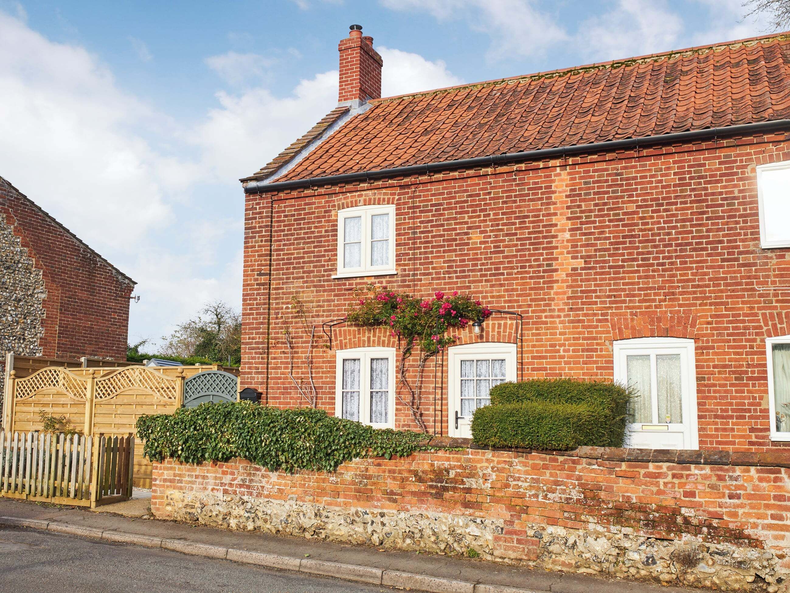 A red brick house with a tiled roof, white windows, and a stone foundation.