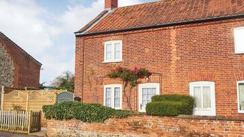 A red brick house with a tiled roof, white windows, and a stone foundation.