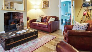 Ein gemütliches Wohnzimmer mit Kamin, Ledersofas, einem großen Spiegel und einem Essbereich, der durch eine offene Tür erkennbar ist.