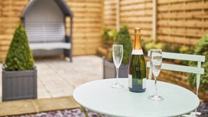 Ein runder Tisch mit zwei Weingläsern und einer Champagnerflasche in einem Garten.