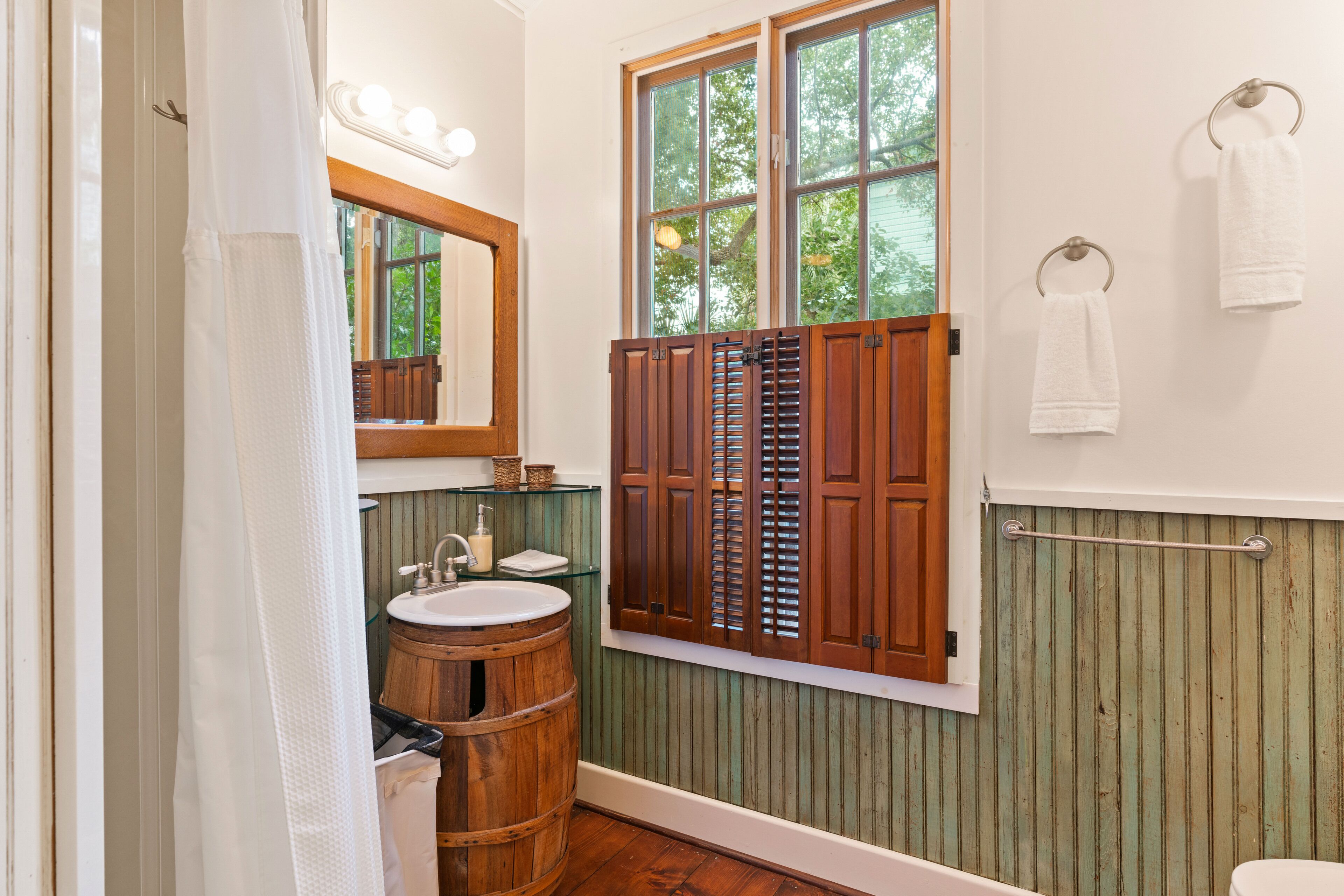 A bathroom with a wooden barrel sink, a window with shutters, and a towel rack.