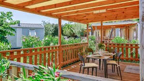 Eine Holzdielen-Terrasse mit Esstisch, umgeben von einem Holzgeländer und verschiedenen Pflanzen.