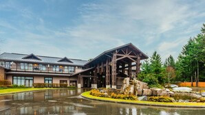 A modern building with a covered outdoor area, a reflective water feature, and a landscaped garden. - Ocean Front Resort - 1 Bedroom Suite (Parksville)