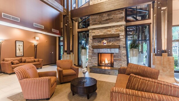 A modern living room with a stone fireplace, large windows, and a mix of sofas and armchairs. - Ocean Front Resort - 1 Bedroom Suite (Parksville)