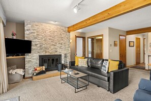 A living room with a stone wall, a fireplace, a leather sofa, and a television.
