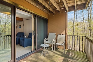 A balcony with a wooden deck, a glass door leading to a room with two blue chairs and a small table.