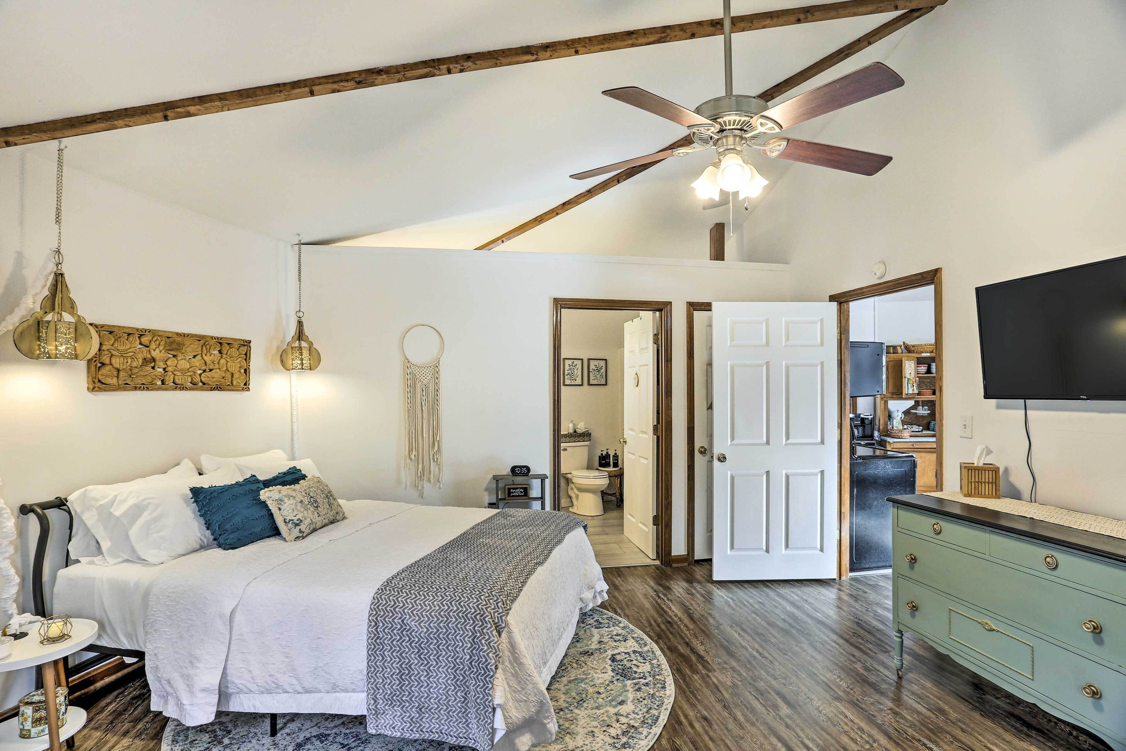 Une chambre à coucher comprenant un lit, une table de chevet, un ventilateur de plafond et donnant sur la salle de bain.
