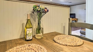 Een houten tafel met een fles wijn, een vaas met bloemen en geweven placematen.