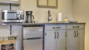 Een kleine keuken met een koelkast van roestvrij staal, een magnetron, een koffiezetapparaat en een wastafel met kraan.