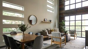 A spacious living room with a dining area, large windows, and a rustic brick wall. - CENTRAL Modern Condo!! 4 Mins to Airport, Mins to Downtown Bozeman! (Belgrade)