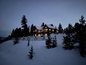 A large, multi-story lodge with a snow-covered roof, surrounded by tall pine trees, set against a twilight sky. - BRAND NEW LISTING! Gorgeous Private Big Sky Cabin! (Big Sky)