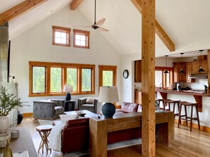 A spacious living area with a high ceiling, wooden beams, and large windows offering a view of the outdoors. - BRAND NEW LISTING! Gorgeous Private Big Sky Cabin! (Big Sky)