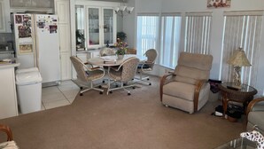 Uma sala de estar ampla com uma mesa de jantar, assentos confortáveis, um ventilador de teto e uma grande janela com cortinas.