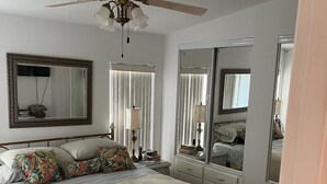 Quarto com cama, ventilador de teto, espelho grande e cômoda.