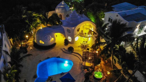 Un edificio único de forma abovedada con piscina, rodeado de palmeras e iluminado por una cálida luz.