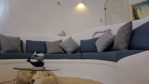 Un salón moderno con un sofá curvo, cojines estampados, una mesa de centro de cristal y una escultura decorativa.