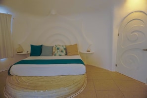 A bedroom with a bed centered against a white wall, flanked by nightstands with lamps.