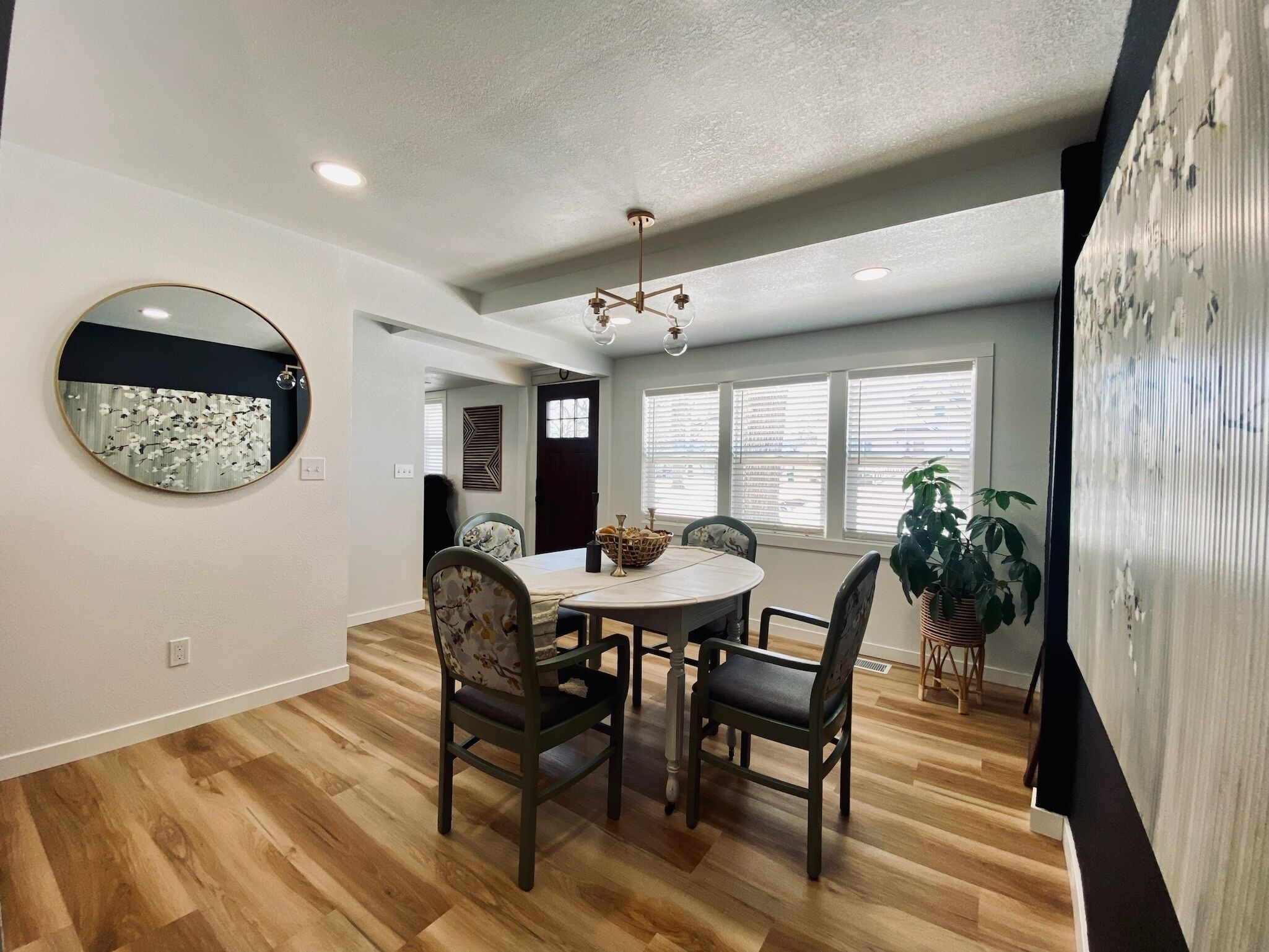 A dining area with a round table, four chairs, a chandelier, and a large mirror on the wall.