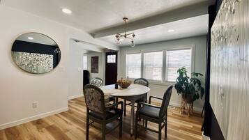 A dining area with a round table, four chairs, a chandelier, and a large mirror on the wall.