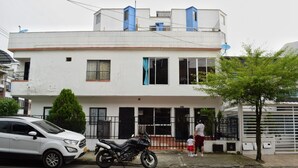 Un edificio de dos pisos con fachada blanca, barandillas negras y un árbol en la parte delantera.