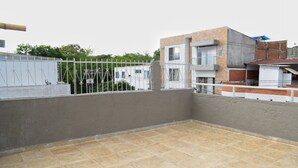Una terraza en la azotea con suelo de baldosas, barandilla de metal y vista de edificios cercanos.
