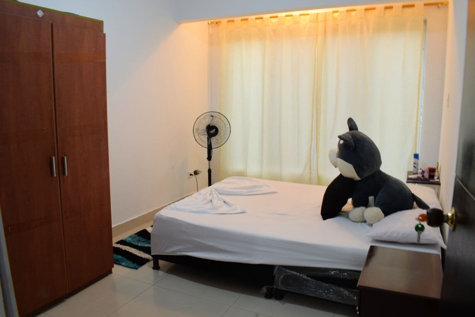 Een slaapkamer met een bed, een ventilator, een kledingkast en een raam met gordijnen.