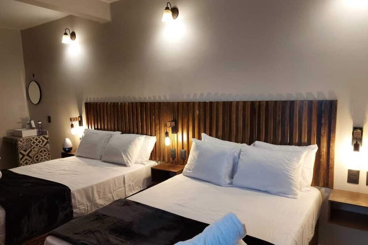 A hotel room with two beds, each with white linens and a wooden headboard. There are bedside lamps and a small table with a lamp on each side.