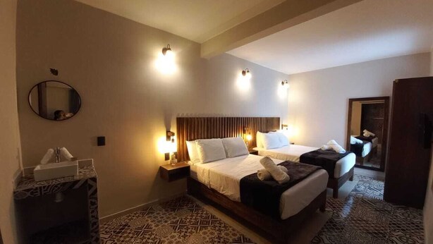 Quarto de hotel com uma cama grande, duas mesinhas de cabeceira, um espelho e carpete estampado.