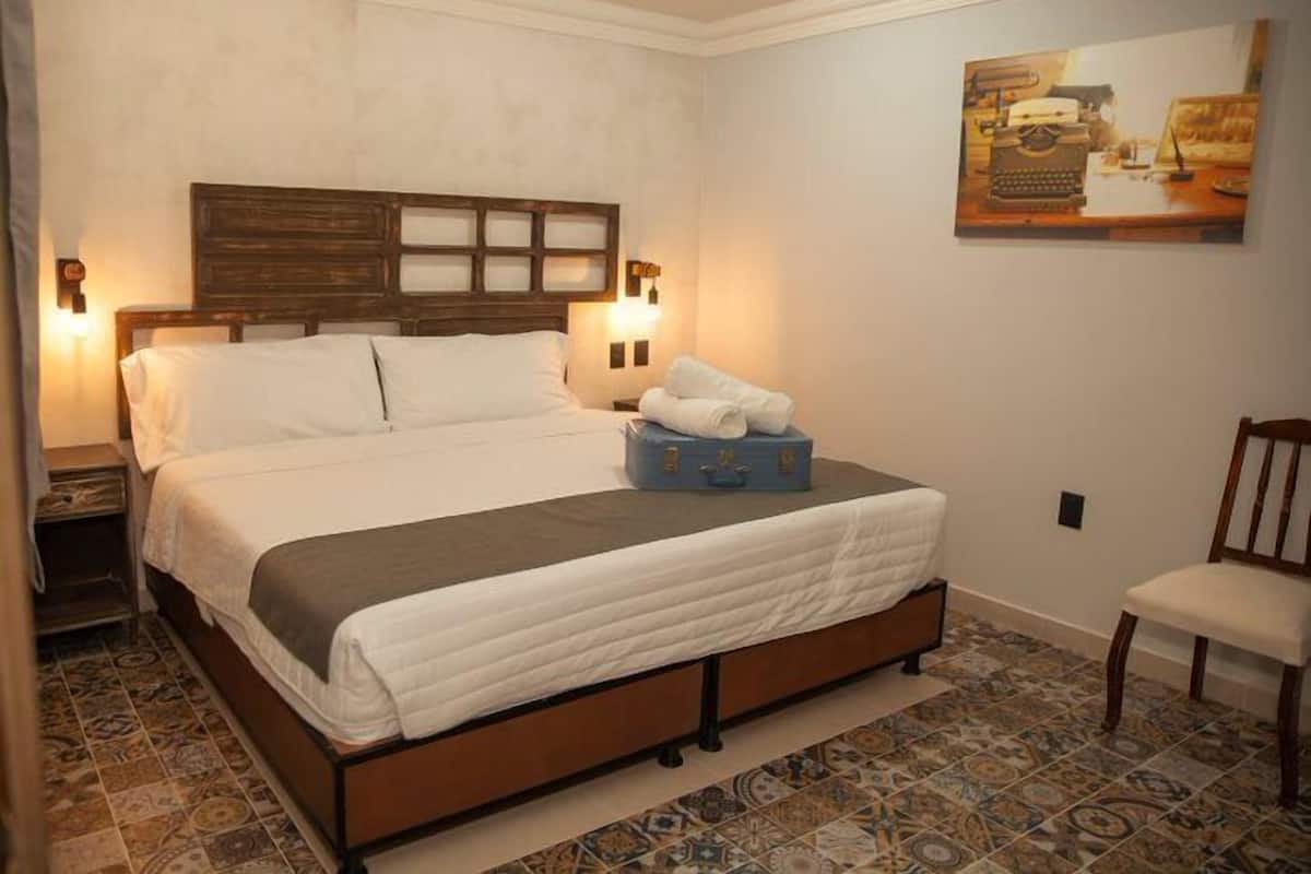 A neatly made bed with a wooden headboard, a nightstand, a chair, and a suitcase on the bed.