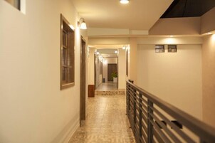 Um corredor com piso estampado, moldura de porta de madeira e corrimão à direita.