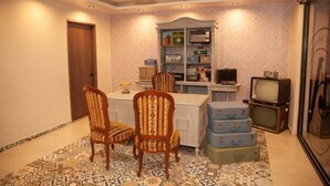 Quarto com uma mesa de jantar, duas cadeiras, uma televisão e uma estante com diversos objetos.