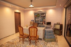 Quarto com uma mesa de jantar, duas cadeiras, uma televisão e uma estante com diversos objetos.