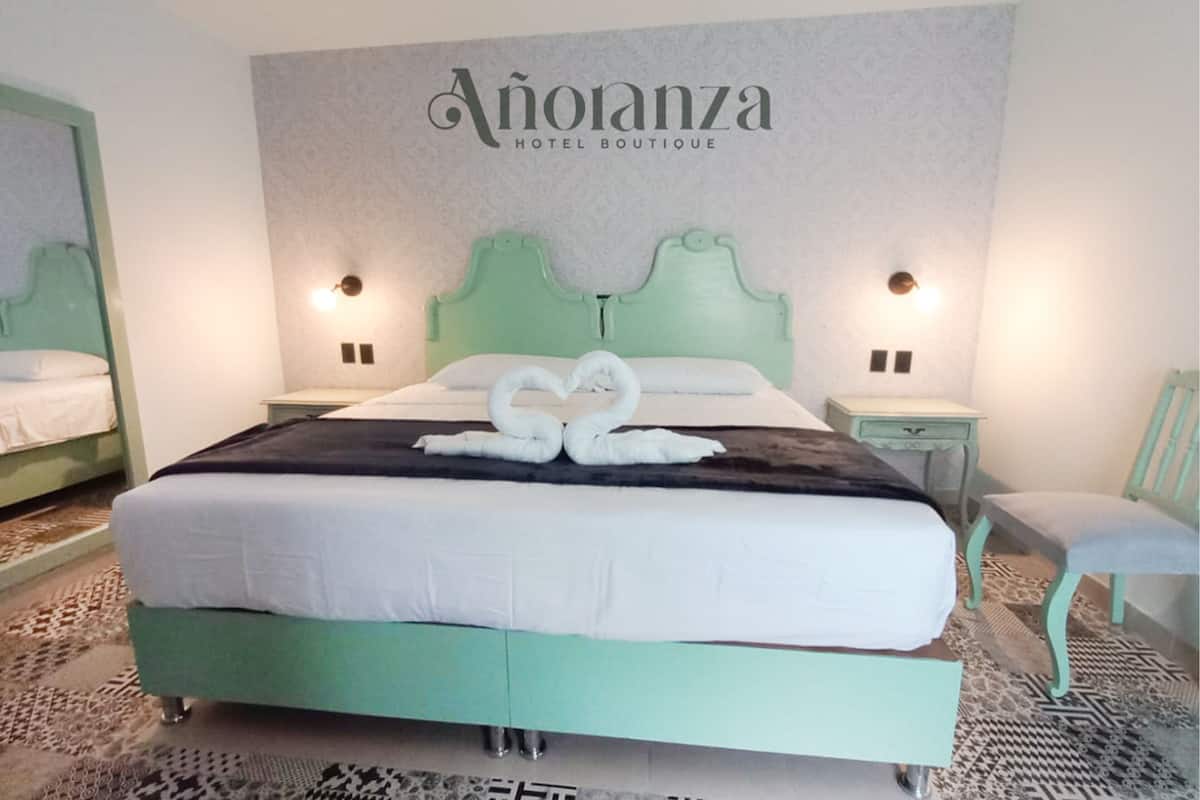 A hotel room with a bed, two bedside tables, a chair, and a wall with the hotel's name.