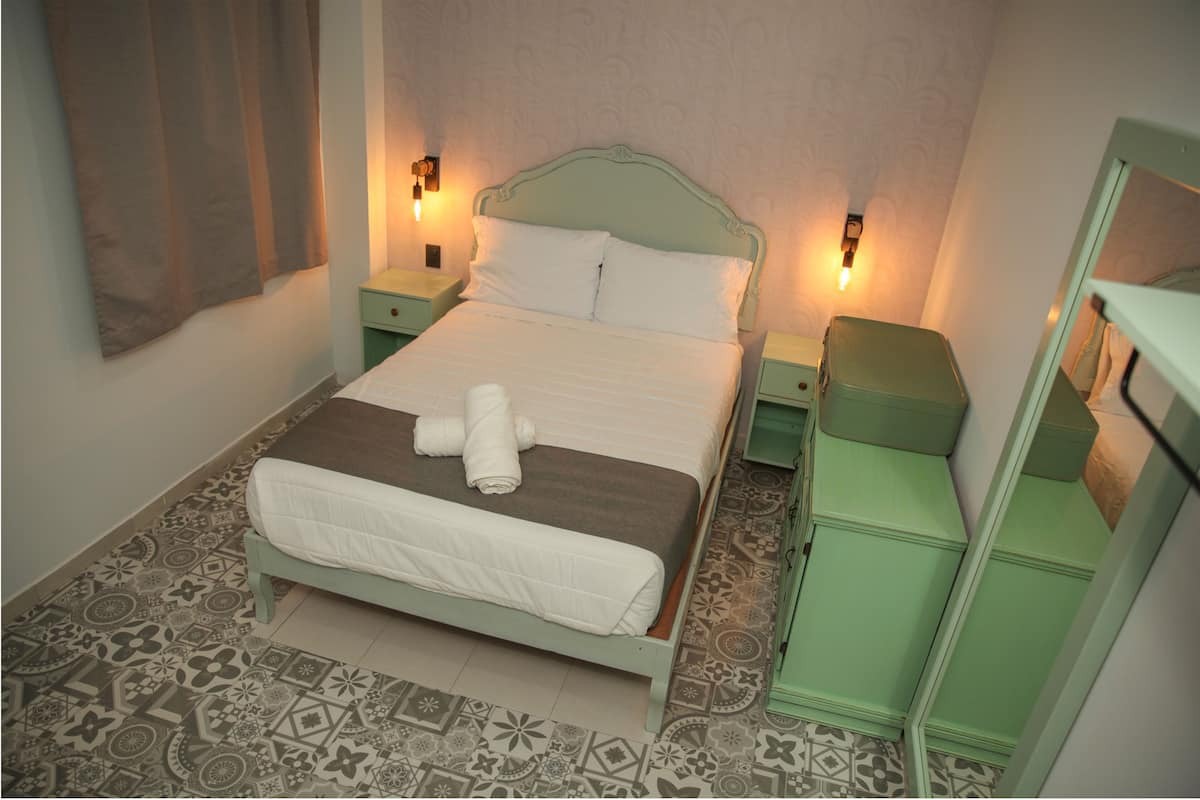 A neatly made bed with a white duvet and brown blanket, two bedside tables with lamps, a green nightstand, and a green dresser with a mirror.