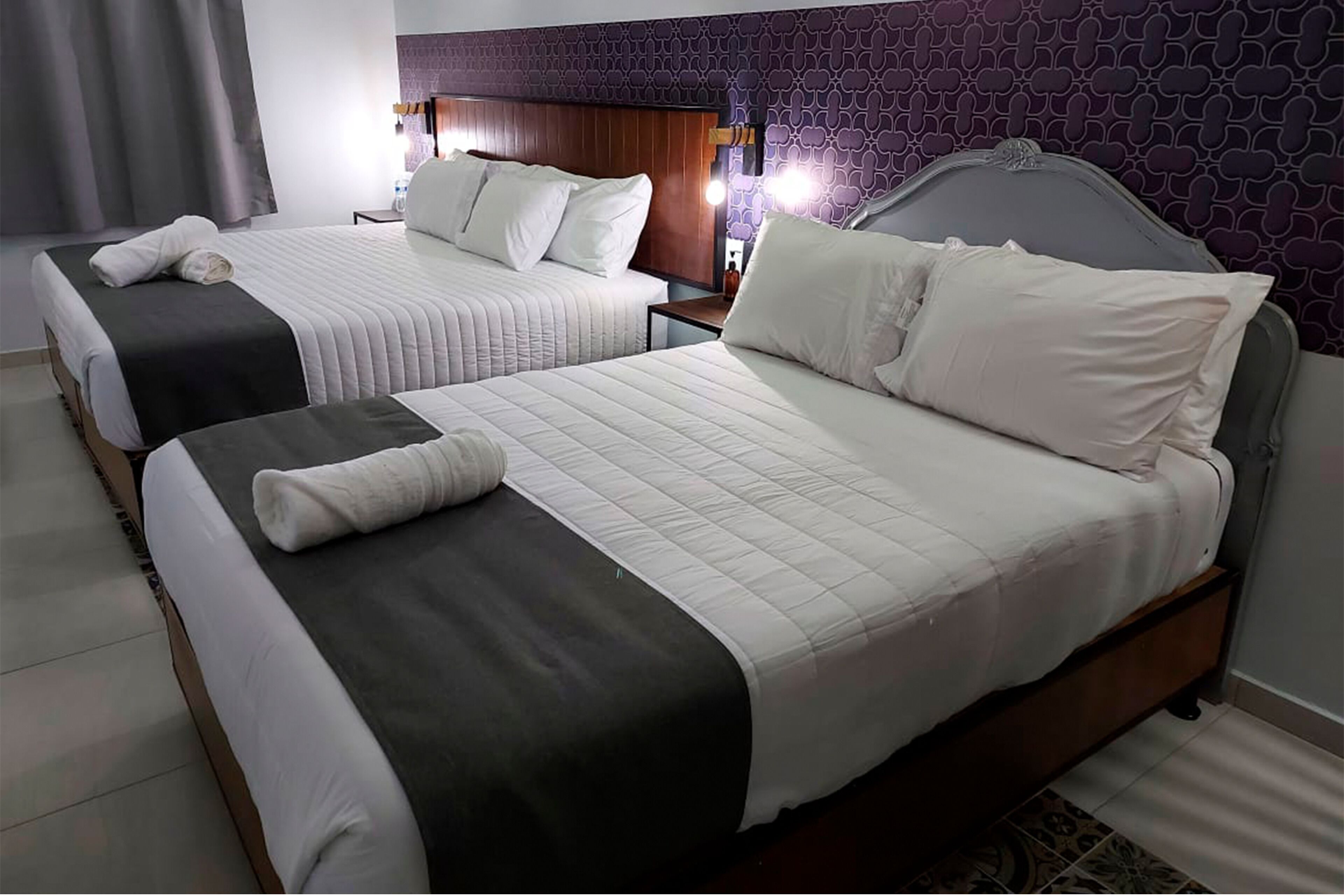 Ein Hotelzimmer mit zwei Betten, jedes mit einer dunkel und hellen Bettdecke, weißen Kissen und einem ordentlich gefalteten Handtuch.