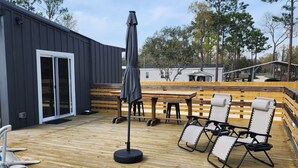 Une terrasse en bois avec des meubles d’extérieur, notamment des chaises longues et une table, et une piscine sur le côté gauche.
