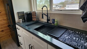 Une cuisine moderne avec un plan de travail noir, des armoires blanches et une fenêtre donnant sur des arbres et des maisons.
