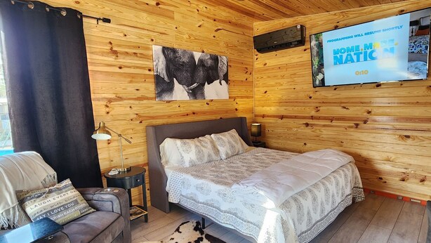 Une pièce chaleureuse, avec des murs en bois, comprenant un lit, un canapé, une télévision et un ventilateur de plafond.