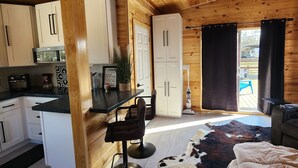 Un intérieur de chalet chaleureux avec des murs en bois, un coin cuisine, un espace repas et un salon agrémenté d’un tapis en peau de vache.