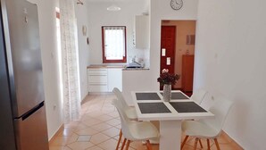A compact kitchen with a refrigerator, a dining table with chairs, and a clock on the wall.