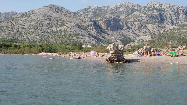 A beach with people sunbathing and swimming, surrounded by rocky mountains.