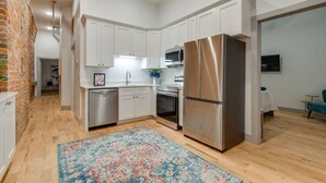 A modern kitchen with white cabinets, stainless steel appliances, and a wooden floor. - Majestic Lofts #302- Balcony over Printers Alley (Nashville)