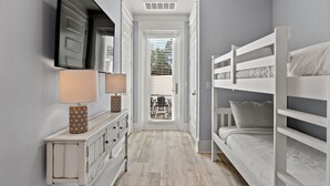 A narrow hallway with a bunk bed, a dresser with two lamps, and a door leading to a balcony.