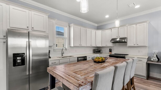 A modern kitchen with white cabinetry, stainless steel appliances, and a wooden island with seating.